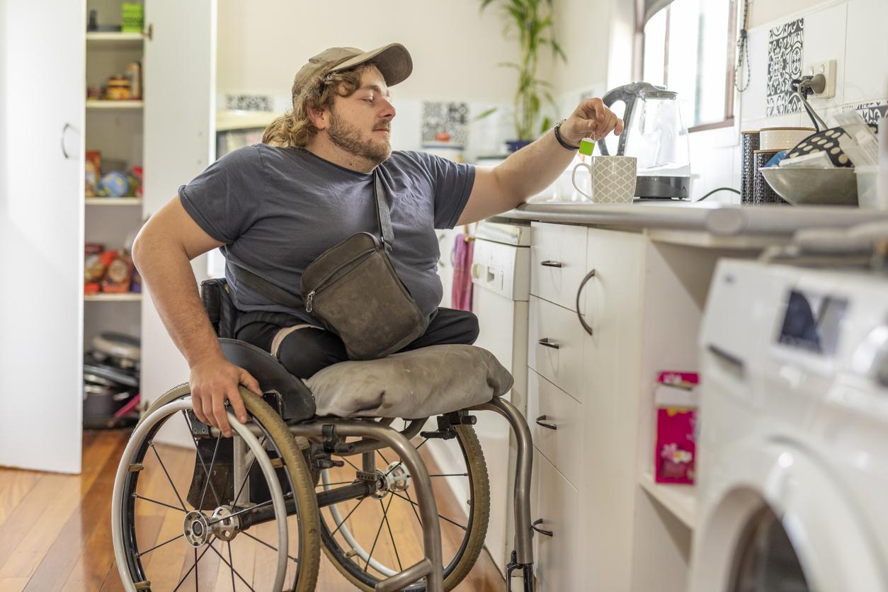 A man with no legs in a wheelchair is making tea in his kitchen.