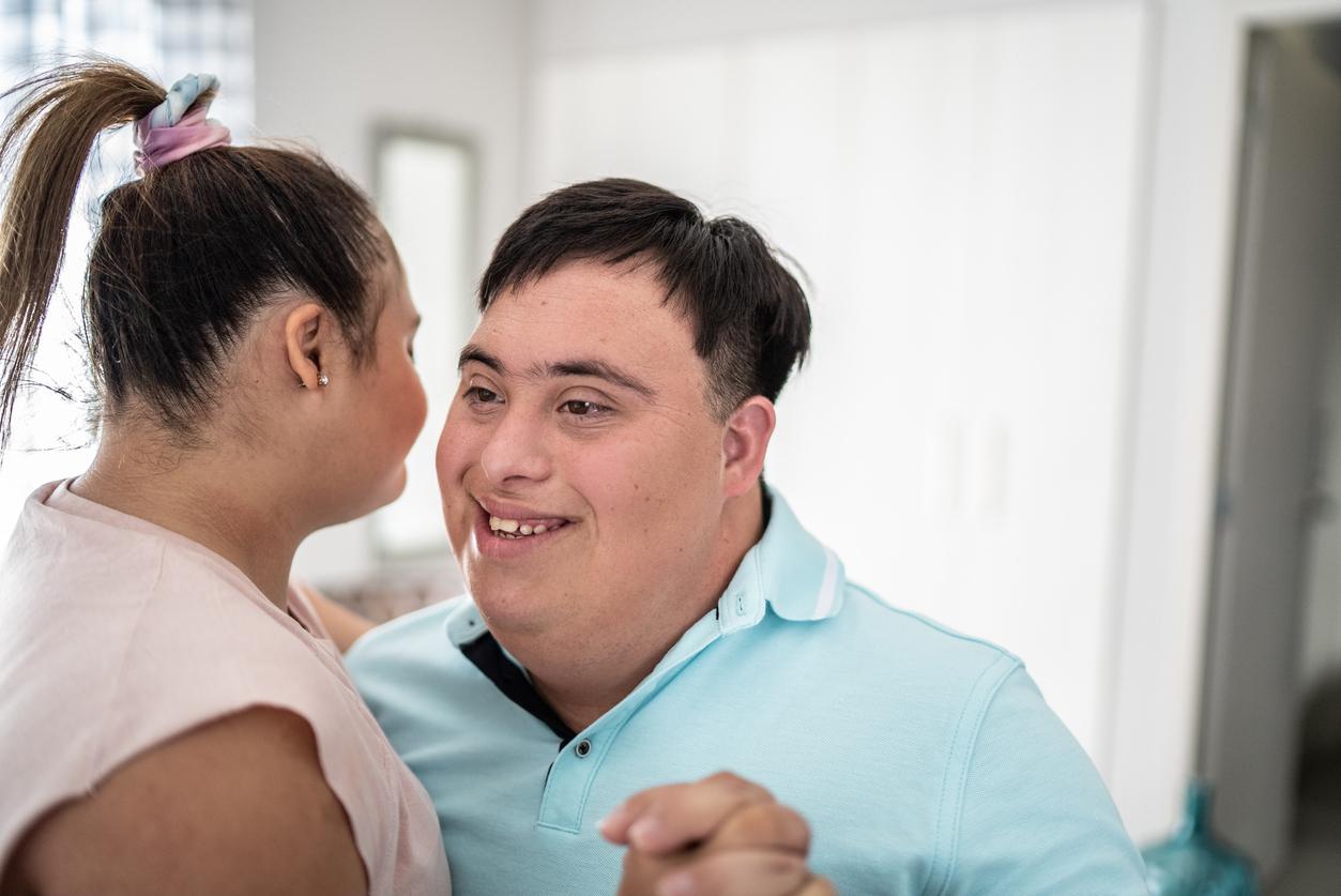 A young man with a developmental disability is smiling and dancing with a young woman.