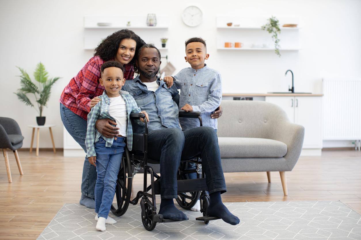 A man in a wheelchair is surrounded his family of two young boys and a woman. They are smiling for the camera.